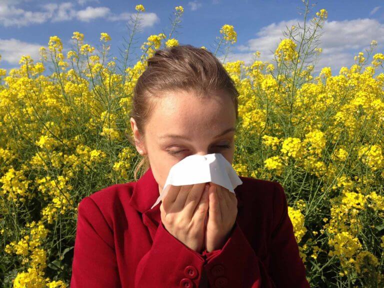 woman sneezing into a tissue with flowers behind her