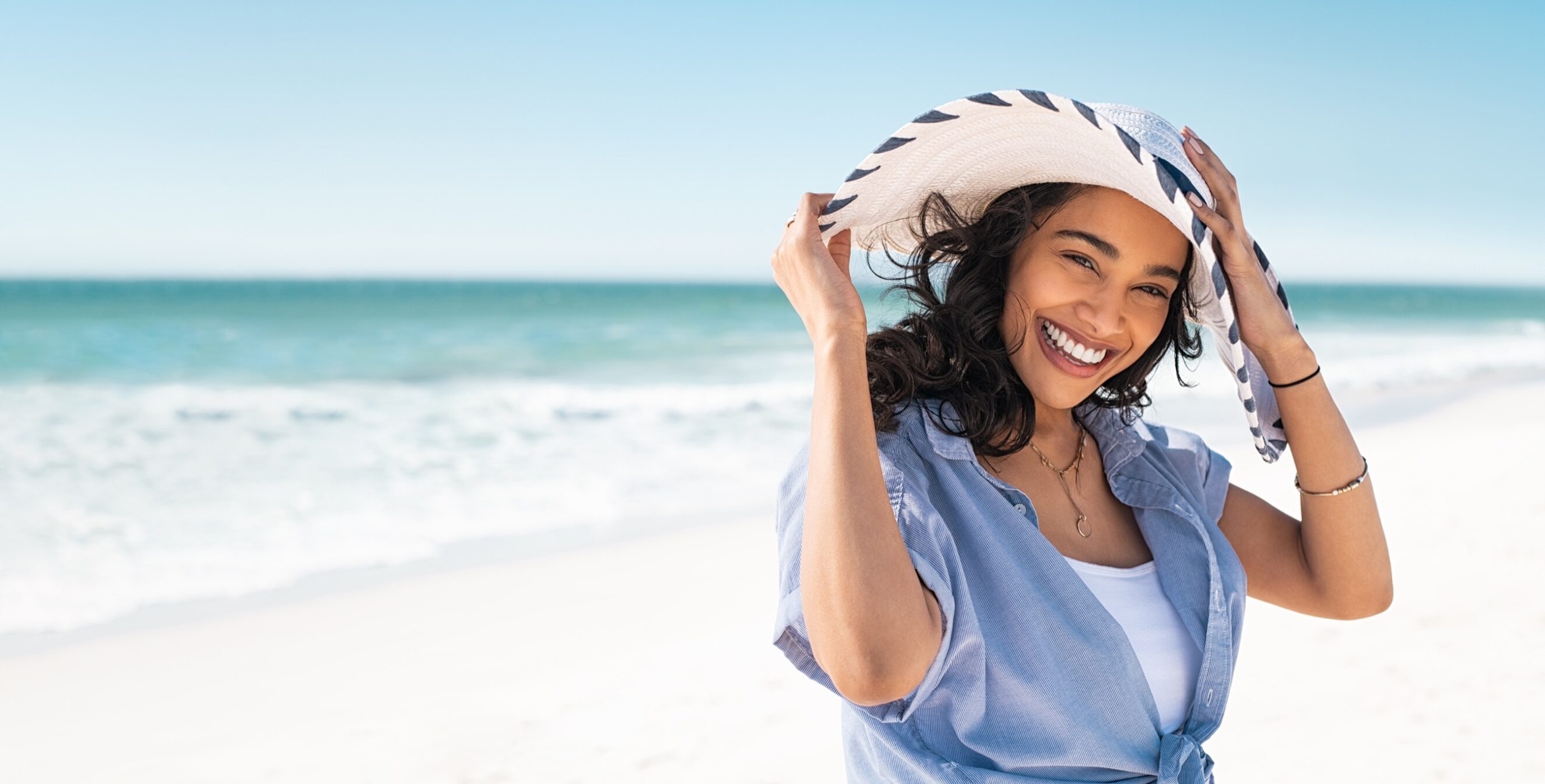 Young smiling woman on vacation enjoy sea breeze wearing straw hat and looking at camera.